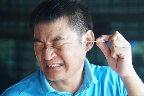 Asian man make face expression during using cotton bud stick to remove earwax. C Stock Photos