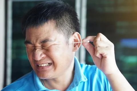 Asian man make face expression during using cotton bud stick to remove earwax. Stock Photos