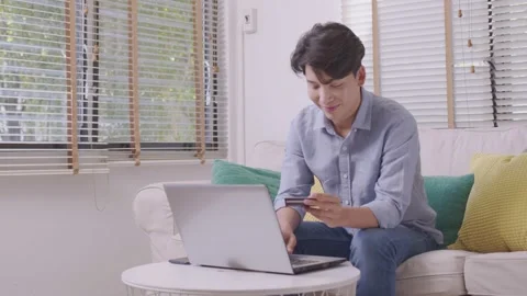 Asian man makes a payment via the internet. On the sofa at home, a shopper sh Stock Footage 167718260