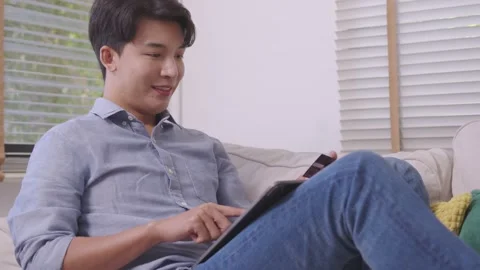 Asian man makes a payment via the internet. On the sofa at home, a shopper sh Stock Footage 167718440