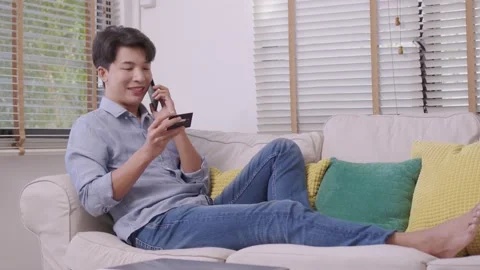 Asian man makes a payment via the internet. On the sofa at home, a shopper sh Stock Footage 167718537