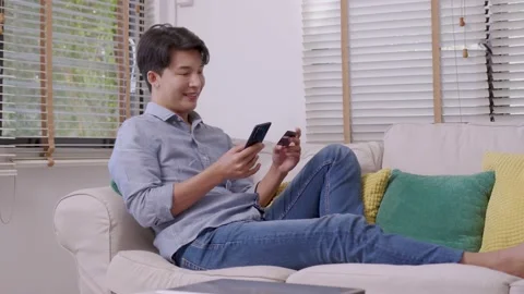 Asian man makes a payment via the internet. On the sofa at home, a shopper sh Stock Footage 167719642