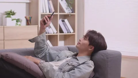 Asian man making facetime video calling with smartphone at home. He's waving  Video stock 172430570