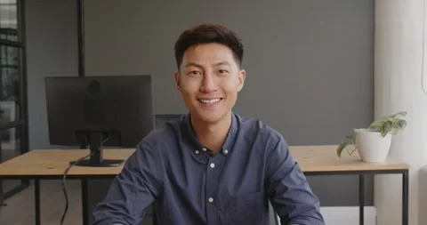 Asian man in office smiling with eyes closed, sitting at desk with computer Stock Footage 346145656