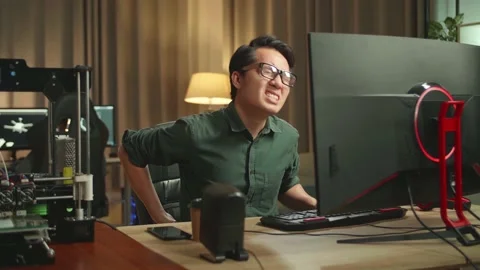 Asian Man Paining His Back While Works On Personal Computer And 3D Printer Stock Footage 158107796