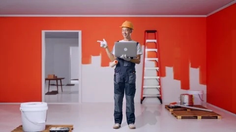 Asian Man Painter Using A Laptop And Pointing To Side With Painting Wall In Room Stock Footage 283075648