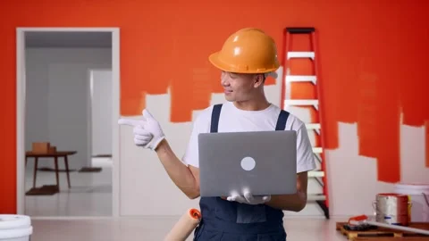 Asian Man Painter Using A Laptop And Pointing To Side With Painting Wall In Room Stock Footage 283076528
