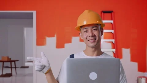 Asian Man Painter Using A Laptop And Pointing To Side With Painting Wall In Room Stock Footage 283077710