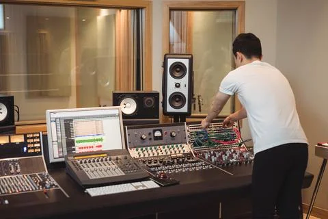 Asian man plugging colorful patch cables into mixing console bay in studio Stock Photos