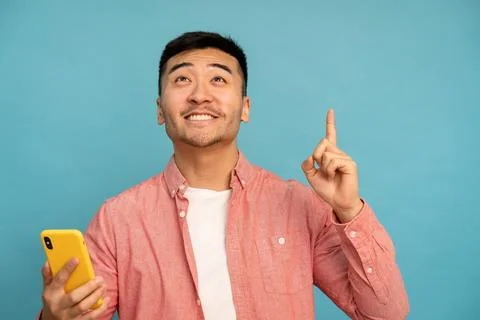 Asian man pointing upward while holding phone. Stock Photos