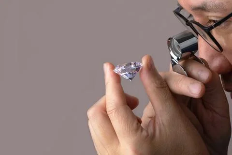 Asian man in the process of evaluating a round cut diamond using a magnifying Stock Photos