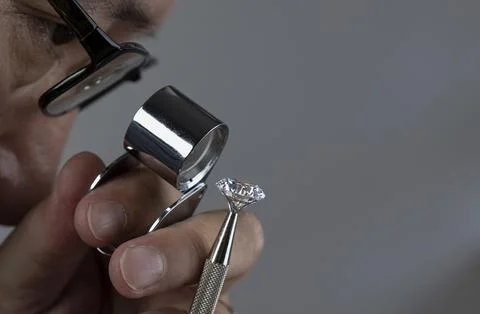 Asian man in the process of evaluating a round cut diamond using a magnifying Stock Photos