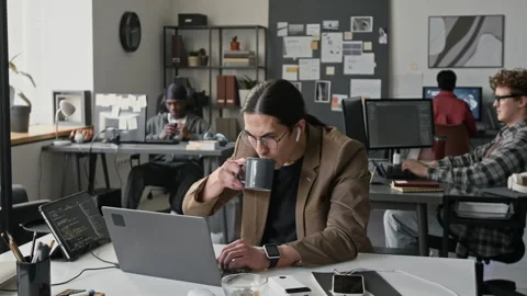 Asian Man Programming on Laptop and Drinking Coffee in Office 動画素材 336712337