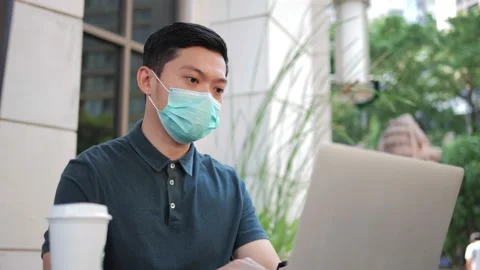 Asian man with protective face mask is working with laptop at outdoor cafe Stock Footage 156439357