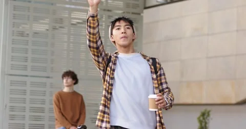 Asian man pulling suitcase and holding coffee while walking forecourt, raising Stock Footage 336535301