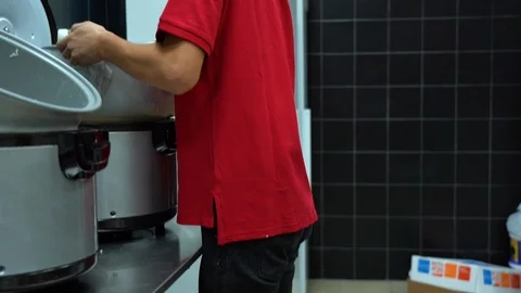 Asian man pulls and carries away a pan of hot rice from open silver rice cooker. Stock Footage 119979177