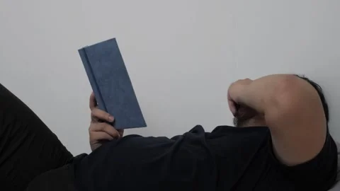 Asian man reading book in bed before sleep, minimalist sparse room with sin.. Stock Footage 295987073