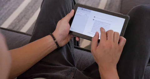 Asian man reading messages while tapping tablet on sofa, wearing light shirt, Stock Footage 344318535