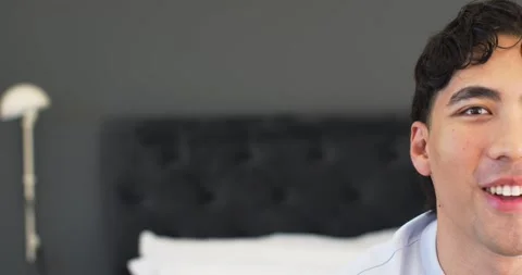 Asian man responding to off-camera cue, approaching bed headboard, making eye Stock Footage 340070541