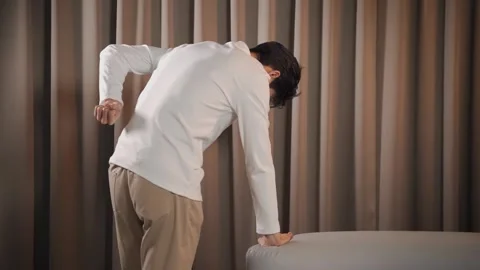 Asian man rubbing lower back while standing by sofa experiencing sharp spin.. Stock Footage 337764970