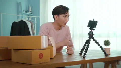 An Asian man is showing clothes in front of smartphone  live streaming at his Видео 172007715