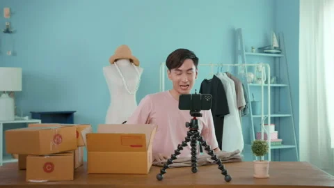 An Asian man is showing clothes in front of smartphone  live streaming at his Vídeo Stock 172007865