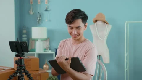 An Asian man is showing clothes in front of smartphone  live streaming at his 库存影片 172007897