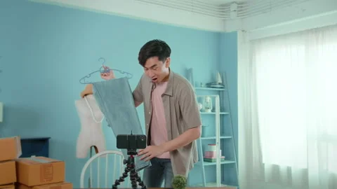 An Asian man is showing clothes in front of smartphone  live streaming at his Stock-Footage 172008186