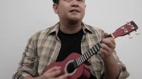 Asian man singing while playing ukulele Stock Footage 293532446
