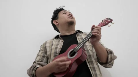 Asian man singing while playing ukulele Stock Footage 293532515