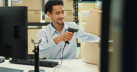 Asian man sit front desk computer use barcode machine scan record online data. Stock Footage 229646383
