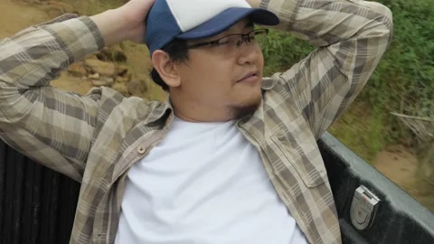 Asian man sitting in the back of pickup truck, outdoor safari trip adventure  Stock Footage 150789023
