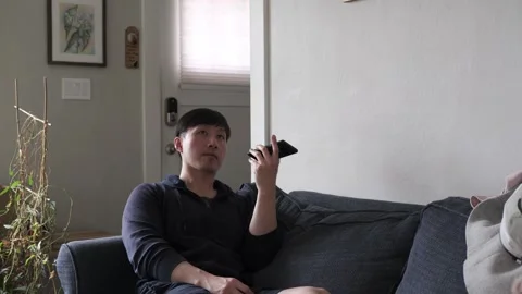 Asian man sitting on a couch using his cell phone Stock-Footage 303256433