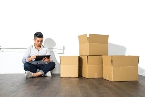 Asian man sitting on floor using his Tablet with boxes 스톡 사진