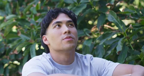 Asian man sitting in light gray t-shirt, resting forearms on surface, looking up Stock Footage 336716491