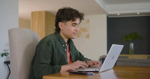 Asian man sitting at table typing on laptop reading message using mouse sipping Stock Footage 347726687
