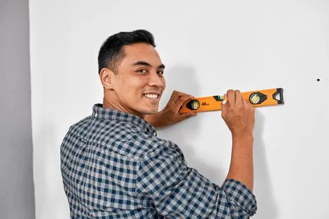 An Asian man smiles while using spirit level against wall doing home DIY Stock Photos