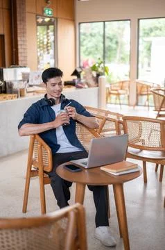 Asian man smiling and drinking iced coffee while watching online media on l.. Stock Photos