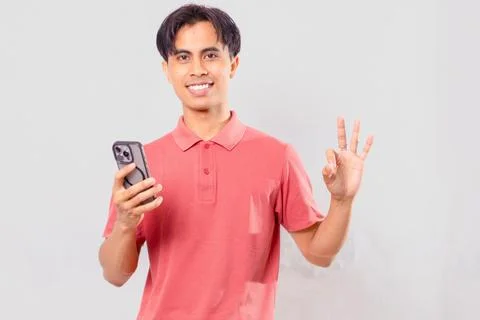 Asian man smiling at camera while holding phone showing three fingers, perf.. Stock Photos