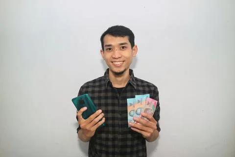 Asian man smiling happy while holding mobile phone and money Stock Photos