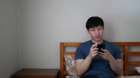 Asian man smiling while on his phone using social media Stock Footage 248665445
