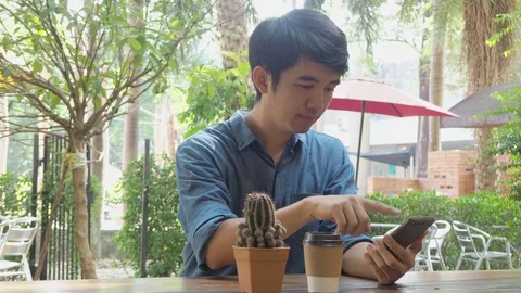 Asian man smiling while reading his smartphone with a cup of coffee Stock Footage 118362989