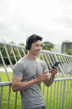 Asian man smiling while using smartphone with wireless headphones outdoors Stock Photos