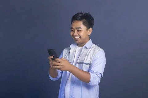 Asian man smiling while using a smartphone, looking at the screen with a ha.. Stock Photos