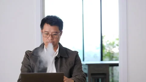 Asian man smokes electronic cigarette while working at home Stock Footage 252781653