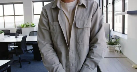 Asian man standing in open office in khaki from clasped hands, crossing arms Stock Footage 342284392