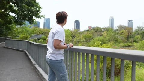 Asian Man Stretching on Elevated Walkway Overlooking Bangkok City Skyline Stock Footage 336523578