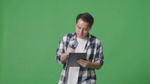 Asian Man Taking Note On Tablet While Walking On Green Screen In The Studio Stock Footage 248006134