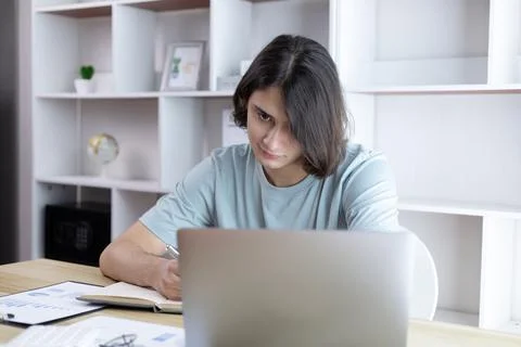 Asian man taking notes in notebook while studying online in laptop at home, V Stock Photos