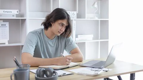 Asian man taking notes in notebook while studying online in laptop at home, V 스톡 사진